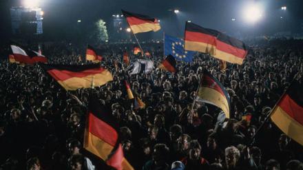 Menschen feiern die Deutsche Wiedervereinigung, dabei schwenken sie deutsche Flaggen und Fahnen. Aufgenommen in Berlin am 03.10.1990.