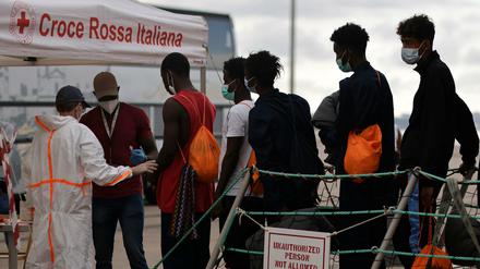 Migranten gehen von Bord der „Ocean Viking“ und werden von Mitgliedern des italienischen Roten Kreuz im Hafen von Taranto in Empfang genommen.