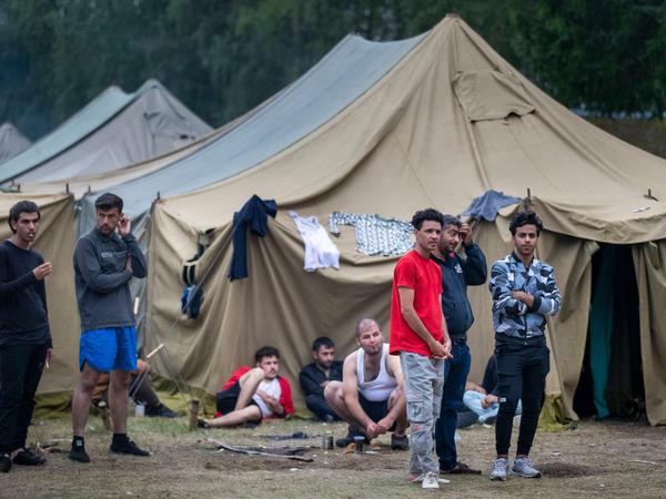 Flüchtlinge stehen vor Zelten auf dem Gelände eines neu errichteten Flüchtlingslagers auf einem Truppenübungsplatz bei Vilnius. 