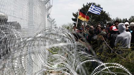 Flüchtlinge mit einer griechischen und einer deutschen Nationalfahne am Grenzzaun zu Mazedonien am Montag. 