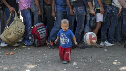 Flüchtlinge stehen in Serbien Schlange, während ein Kind mit dem Ball spielt.
