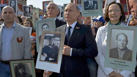 Kremlchef Wladimir Putin steht an der Spitze einer Demonstration, bei der Kinder und Enkel Fotos von Sowjetsoldaten aus dem Zweiten Weltkrieg hochhalten.