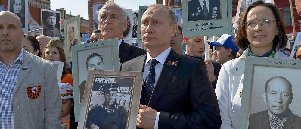 Kremlchef Wladimir Putin steht an der Spitze einer Demonstration, bei der Kinder und Enkel Fotos von Sowjetsoldaten aus dem Zweiten Weltkrieg hochhalten.