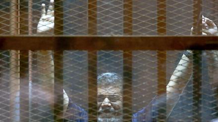 Ägyptens gestürzter Präsident Mohamed Mursi winkt aus dem Angeklagtenkäfig.