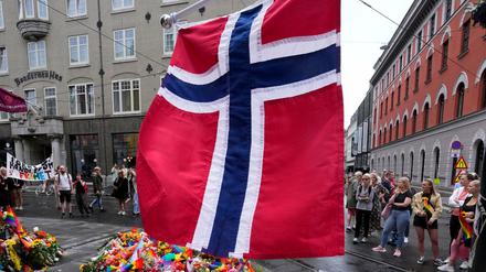 Eine norwegische Nationalflagge weht über Blumen und und kleinen Regenbogenfahnen am Tatort.
