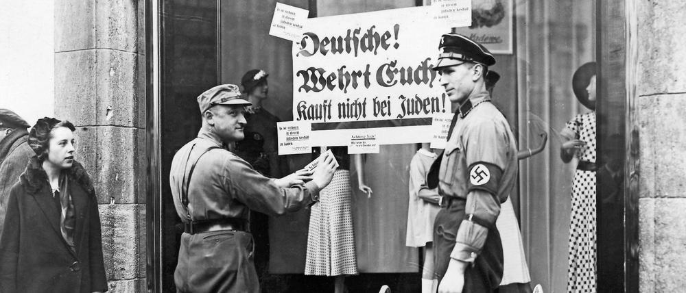 Am Anfang stand die Ausgrenzung: Ein SA- und SS-Mann bekleben 1933 in Berlin das Schaufenster eines Textilgeschäftes mit Boykott-Plakaten.