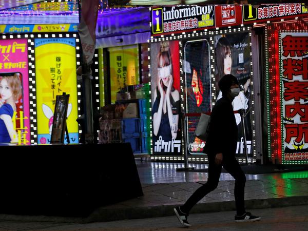 Ein junger Mann mit Maske läuft an einer Bar im Ausgehviertel Kabukicho in Tokio vorbei.