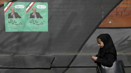 Im Iran geht eine Frau an einem Wahlkampfplakat vorbei. 