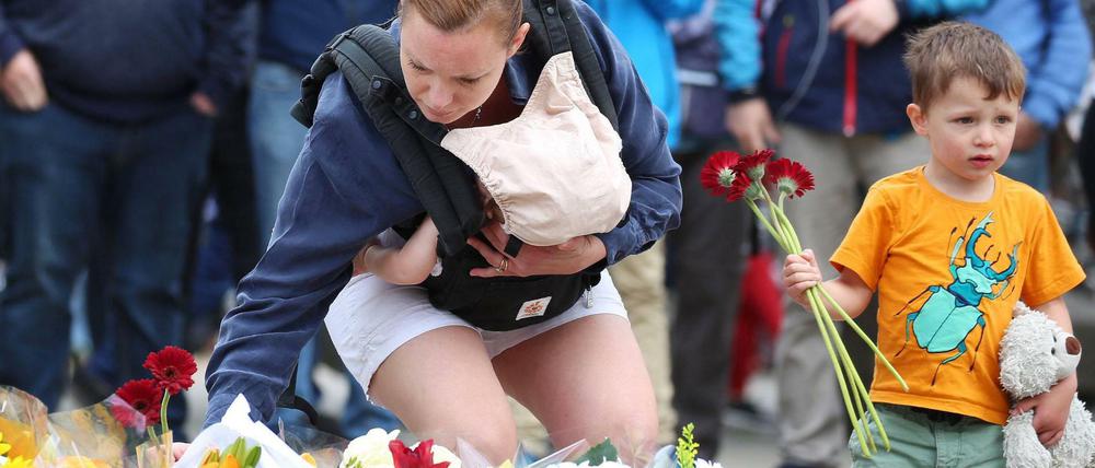 Eine Mutter mit einem Baby im Arm legt an der London Bridge Blumen nieder.
