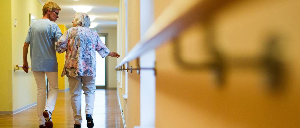 Eine Pflegekraft geht in einem Pflegeheim mit einer älteren Dame über einen Korridor. 