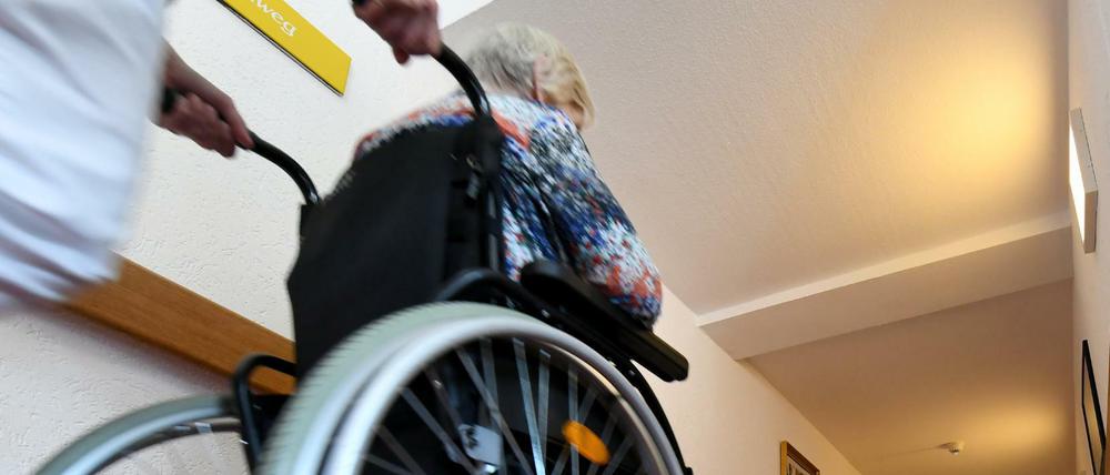Eine Pflegerin schiebt eine ältere Dame im Rollstuhl über einen Flur in einem Seniorenpflegeheim. 