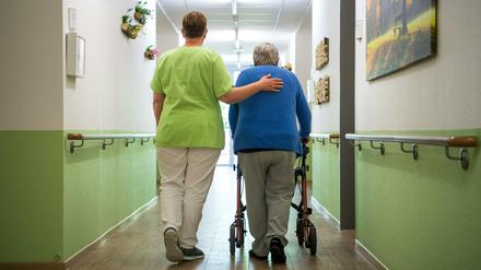 Eine Pflegefachkraft geht mit einer Bewohnerin durch das Seniorenheim.