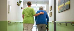 Eine Pflegefachkraft geht mit einer Bewohnerin durch das Seniorenheim.