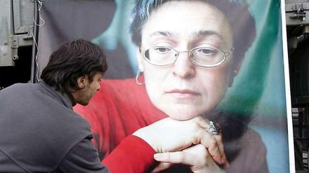 Ein Mann legt an einem großen Porträtfoto von Anna Politkowskaja in Moskau eine Nelke nieder.