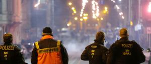 Böllerverbot: Polizisten und ein Rettungssanitäter stehen an einer Kreuzung und schauen auf ein Feuerwerk. (Archivbild)