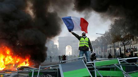 Ein Demonstrant mit einer gelben Weste schwenkt die französische Flagge. Im Hintergrund der Arc de Triomphe.