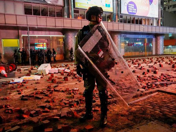 Ein Polizist mit Schutzschild steht am 1. Januar auf einer Straße, die mit Pflastersteinen übersät ist.