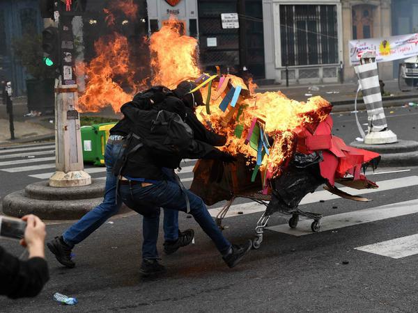 Randalierer schieben am 1. Mai in Paris einen brennenden Einkaufswagen in Richtung Polizeikette.