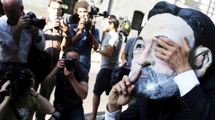Ein Mann mit einer Maske, die Spaniens Premier Rajoy zeigt, hält sich ein Auge zu und legt den Finger an die Lippen. 