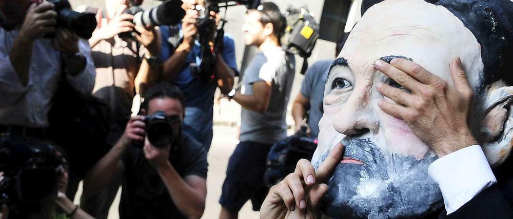 Ein Mann mit einer Maske, die Spaniens Premier Rajoy zeigt, hält sich ein Auge zu und legt den Finger an die Lippen. 