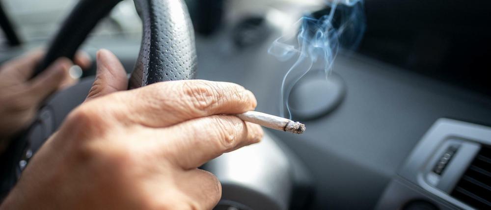 Ein Mann sitzt rauchend am Lenkrad eines Autos.