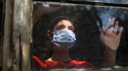 Eine Frau mit Maske schaut aus einem Fenster nach draußen.