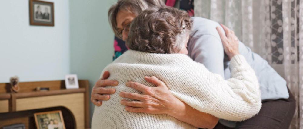 Eine Frau hilft ihrer 93-jährigen Mutter in deren Wohnung beim Aufstehen und Ankleiden.