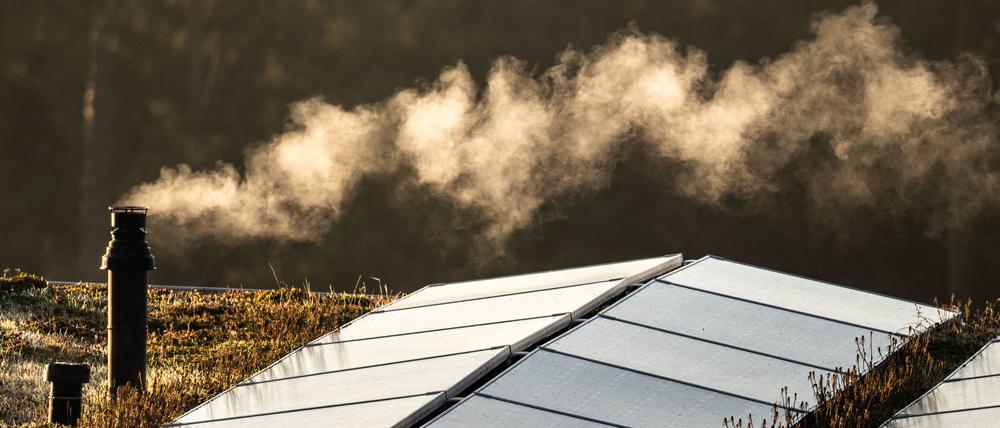 Der Schornstein einer Gastherme für die Heizung und die Warmwasserbereitung dampft am Morgen auf dem Flachdach eines Reihenhauses, auf dem auch eine Solaranlage installiert ist.