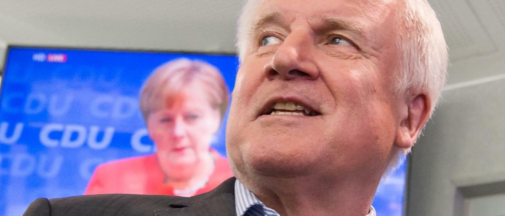 Horst Seehofer läuft auf seinem Weg zur Pressekonferenz an einem Fernseher vorbei, auf dem die Pressekonferenz von Bundeskanzlerin Angela Merkel übertragen wird. 