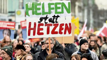 Ein Teilnehmer einer Demonstration hält ein Plakat mit der Aufschrift "Helfen statt Hetzen" in die Höhe (Symbolfoto).