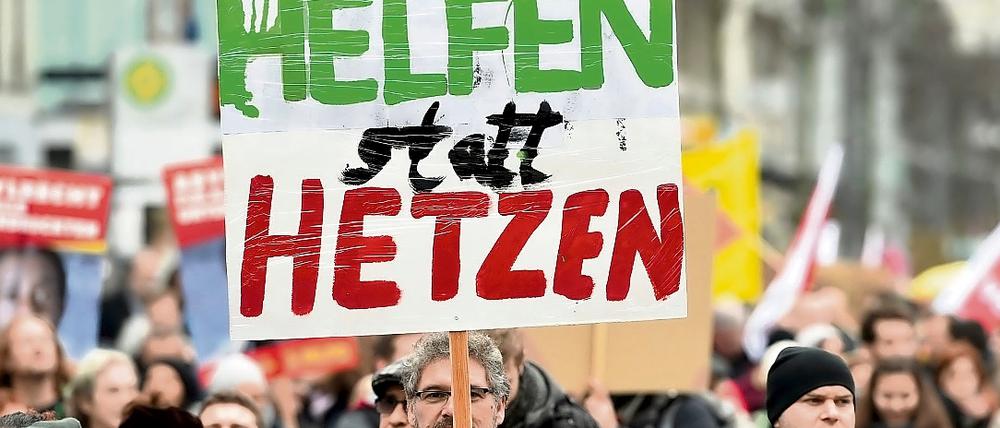 Ein Teilnehmer einer Demonstration hält ein Plakat mit der Aufschrift "Helfen statt Hetzen" in die Höhe (Symbolfoto).