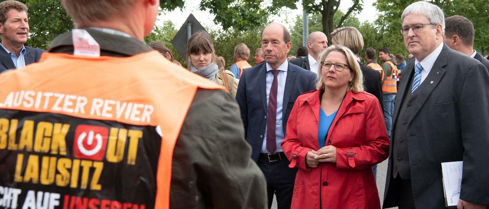 Svenja Schulze und Jörg Steinbach (r, beide SPD) werden von Helmar Rendez (l) und von Demonstranten in orangenen Westen empfangen. 