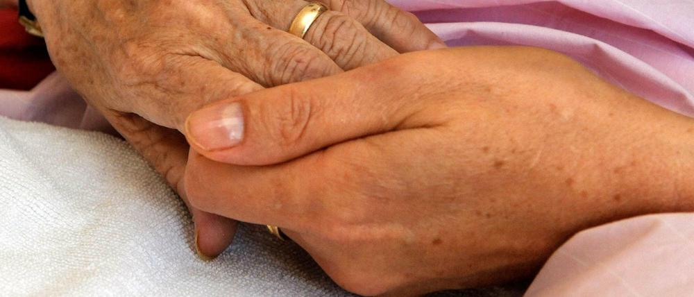 Eine Schwester hält die Hand einer todkranken Bewohnerin eines Hospizes.