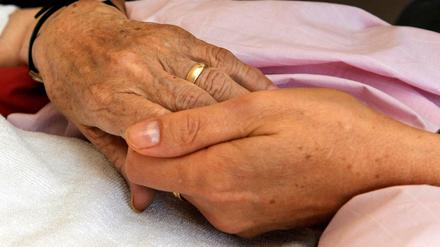 Eine Hospiz-Schwester hält die Hand einer todkranken Bewohnerin.