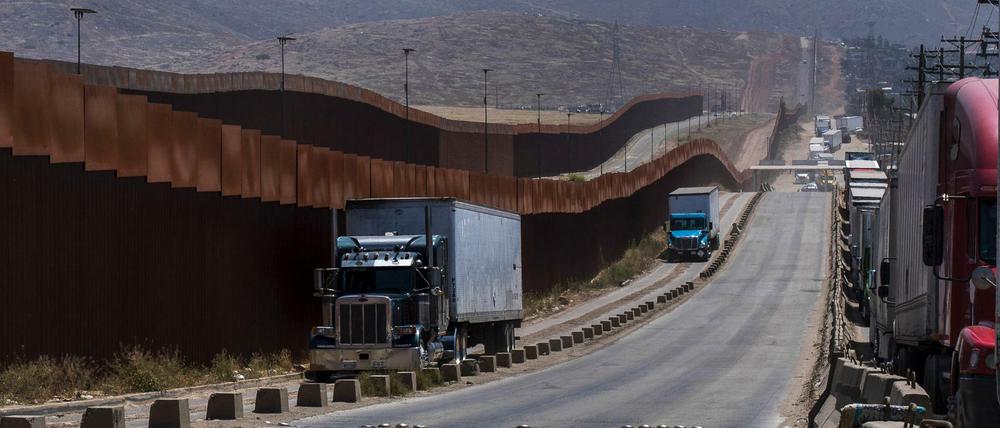 Lastwagen fahren in Tijuana an einem Grenzzaun vorbei, bevor sie über die Grenze in die USA fahren.