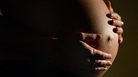 Eine hochschwangere Frau fasst sich mit beiden Händen an ihren Bauch. (Symbolbild)