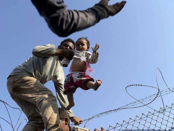 Männer heben ein Baby über den Grenzzaun. Viele hatten nicht dieses Glück. Sie wurden von IS-Terroristen aus dem Grenzgebiet zurückgedrängt.