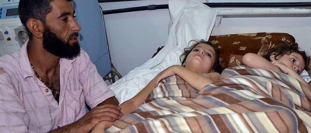 Ein Mann sitzt neben zwei Kindern in einem syrischen Krankenhaus, die nach Angaben von Aktivisten bei einem Giftgaseinsatz der Armee verletzt worden sein sollen.