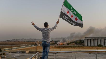 Ein Mann schwenkt die Oppositionsflagge, die ein "Freies Syrien" propagiert, in Akcakale – im Hintergrund die umkämpfte Stadt Tel Abjad.