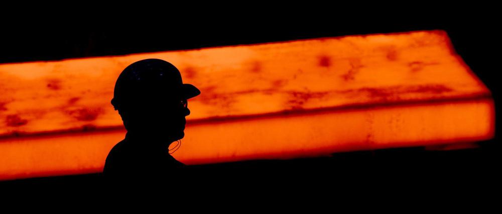 Die Silhouette eines Stahlarbeiters zeichnet sich im Werk der Salzgitter AG vor einer glühenden Bramme ab.