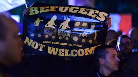 Demonstranten protestieren mit einem Plakat "Refugees not welcome - Bring your families home!" Foto: Martin Schutt/dpa 