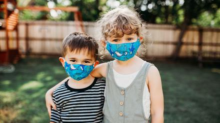 Zwei Kinder tragen ihre Masken im Garten.