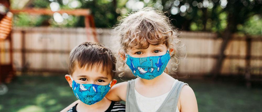 Zwei Kinder tragen ihre Masken im Garten.