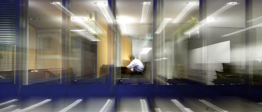 Ein Angestellter sitzt nach Einbruch der Dunkelheit noch in einem Büro am Schreibtisch und arbeitet (Archiv)