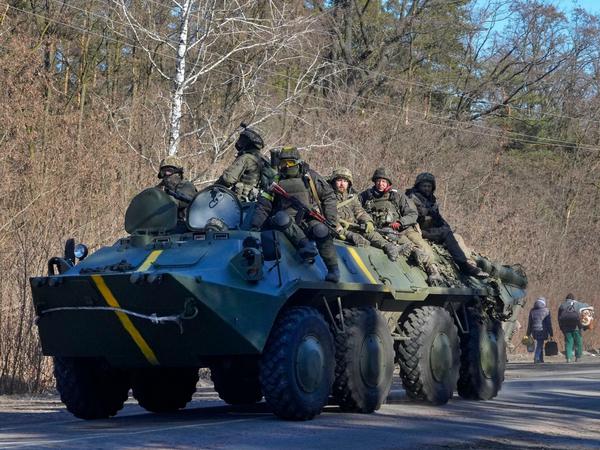 Ukrainische Soldaten auf einem gepanzerten Mannschaftswagen fahren an Menschen vorbei, die ihre Habseligkeiten auf der Flucht vor dem Konflikt tragen, in der Region Wyschgorod in der Nähe von Kiew.
