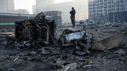 Ein Mann steht auf einem Autowrack inmitten der Zerstörung, die nach dem Beschuss eines Einkaufszentrums in Kiew entstanden ist.
