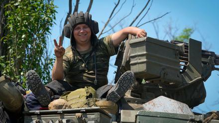 Ukraine, Donezk: Ein ukrainischer Soldat lächelt, während er das Siegeszeichen auf einem Panzer sitzend zeigt. 