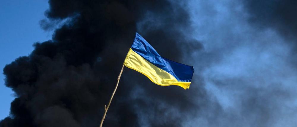 Kiew: Eine ukrainische Flagge weht auf einem Kontrollpunkt, während schwarzer Rauch aus einem Treibstofflager der ukrainischen Armee nach einem russischen Angriff aufsteigt.