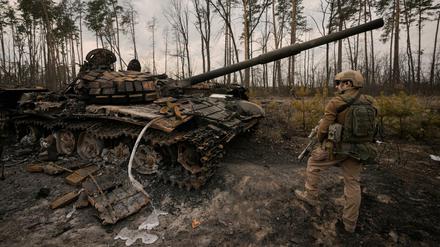 Ein ukrainischer Soldat steht neben einem zerstörten Panzer. 