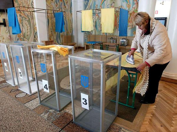 In einem Wahllokal in Kiew bügelt eine Frau Vorhänge in den ukrainischen Landesfarben gelb und blau. 